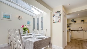A dining area with a table set for four, a kitchen with white cabinets, and a view through a skylight. - 4 Bed in Padstow (oc-p00245) (Padstow)
