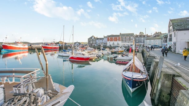 A harbor with boats docked, a walkway along the water, and buildings in the background. - 4 Bed in Padstow (oc-p00245) (Padstow)