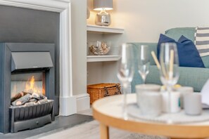 Ein gemütliches Wohnzimmer mit Kamin, einem Regal mit Dekoration und einem Tisch mit Gläsern.