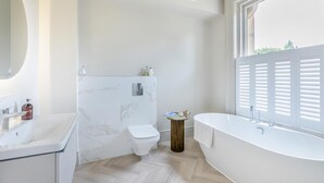 A modern bathroom with a marble wall, a toilet, a sink, a bathtub, and a window with blinds. - 3 Bed in Buxton (oc-p32528) (Buxton)