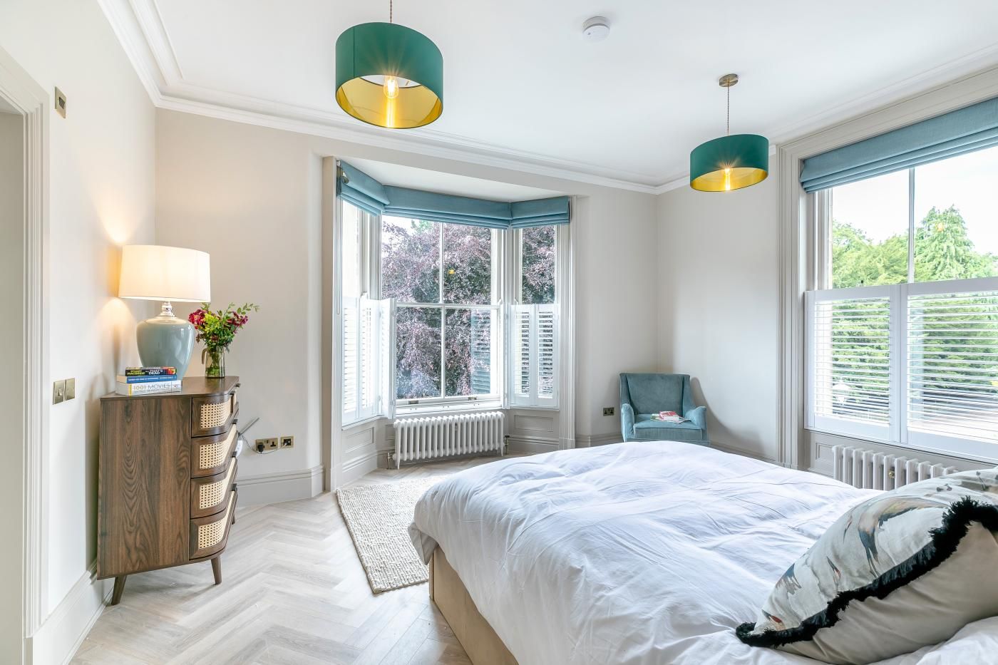 A bedroom with a bed, a dresser, a chair, and two pendant lights.
