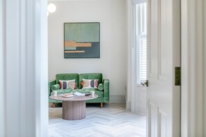 Ein Flur, der zu einem Raum mit einem grünen Sofa, einem Couchtisch und einem Gemälde an der Wand führt.
