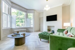 Une pièce dotée d’une baie vitrée, d’une cheminée, d’un canapé vert et d’un téléviseur à écran plat fix é au mur.