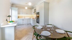A modern kitchen with white cabinets, a dining table set with plates and glasses, and a herringbone-patterned floor. - 3 Bed in Buxton (oc-p32528) (Buxton)