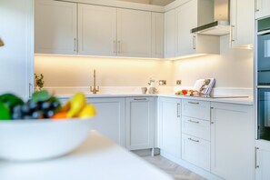 Eine moderne Küche mit weißen Schränken, einer Edelstahl-Dunstabzugshaube und einer Fruchtschale auf der Arbeitsplatte.