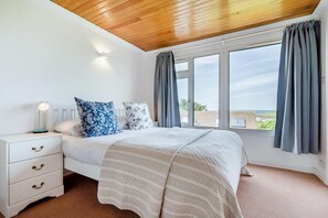 A bedroom with a bed, bedside table, lamp, and large windows with curtains. - 4 Bed in Padstow (oc-p00401) (Trevone)