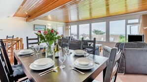 A dining area with a wooden ceiling, large windows, and a table set for four. - 4 Bed in Padstow (oc-p00401) (Trevone)