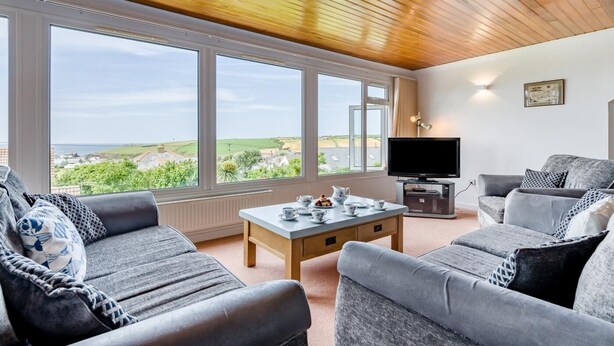 A living room with a large window, a television, and a sofa. - 4 Bed in Padstow (oc-p00401) (Trevone)