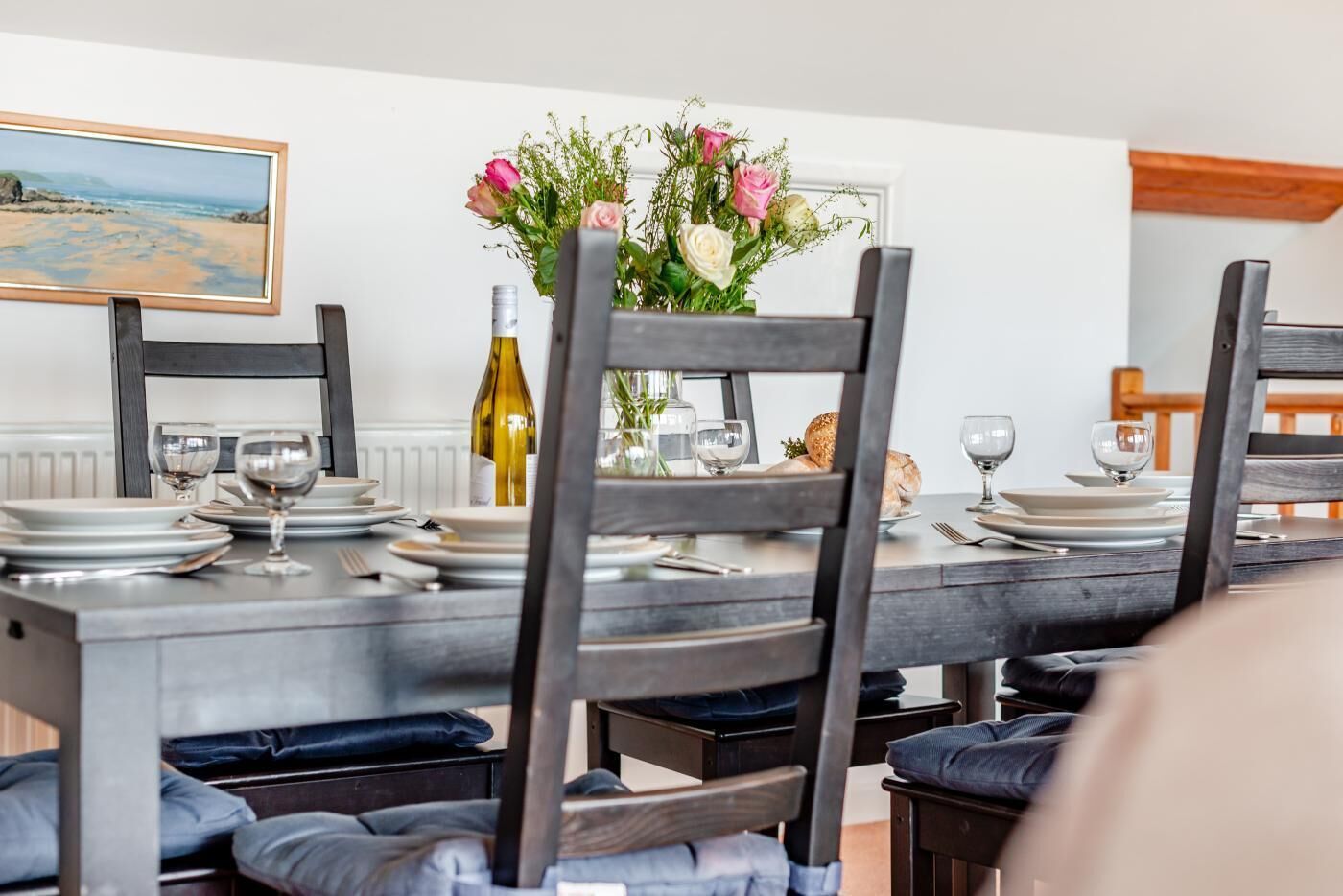 Une table à manger dressée avec des assiettes, des verres et une bouteille, entourée de chaises en bois foncé dotées de coussins bleus.