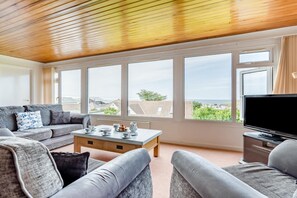 Ein Wohnzimmer mit einer Couch, einem Couchtisch und einem Fernseher, großen Fenstern mit Blick und einer Holzbalkendecke.