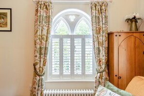 Ein Zimmer mit Fenster, ausgestattet mit weißen Fensterläden, einem Heizkörper darunter und einem Holzschrank mit einer Vase darauf.
