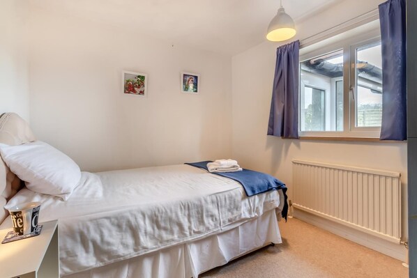 A bedroom with a bed, a window with curtains, a radiator, and two small pictures on the wall.