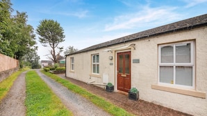 A single-story house with a paved driveway, a front door, and a window with shutters.