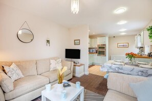 A living room with a sofa, coffee table, TV, and a dining area with a table set for two.