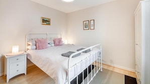A bedroom with a white metal bed frame, a bedside table with a lamp, a drawer, and a wardrobe.