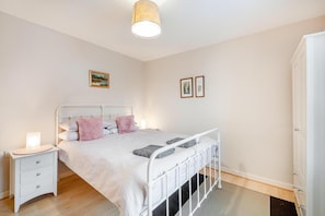 A bedroom with a white metal bed frame, a bedside table with a lamp, a drawer, and a wardrobe.