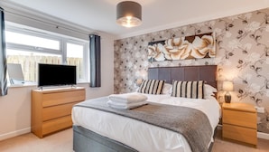 Un dormitorio moderno con una cama grande, un televisor de pantalla plana sobre una cómoda de madera y una ventana con cortinas.