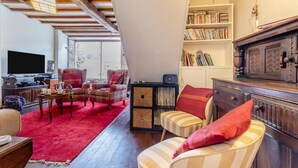 Een woonkamer met een televisie, boekenkasten, een open haard en een rood tapijt.