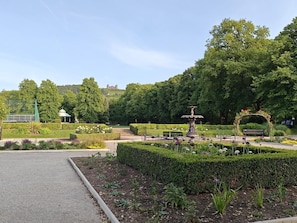A park with a fountain, neatly trimmed hedges, and a gazebo.
