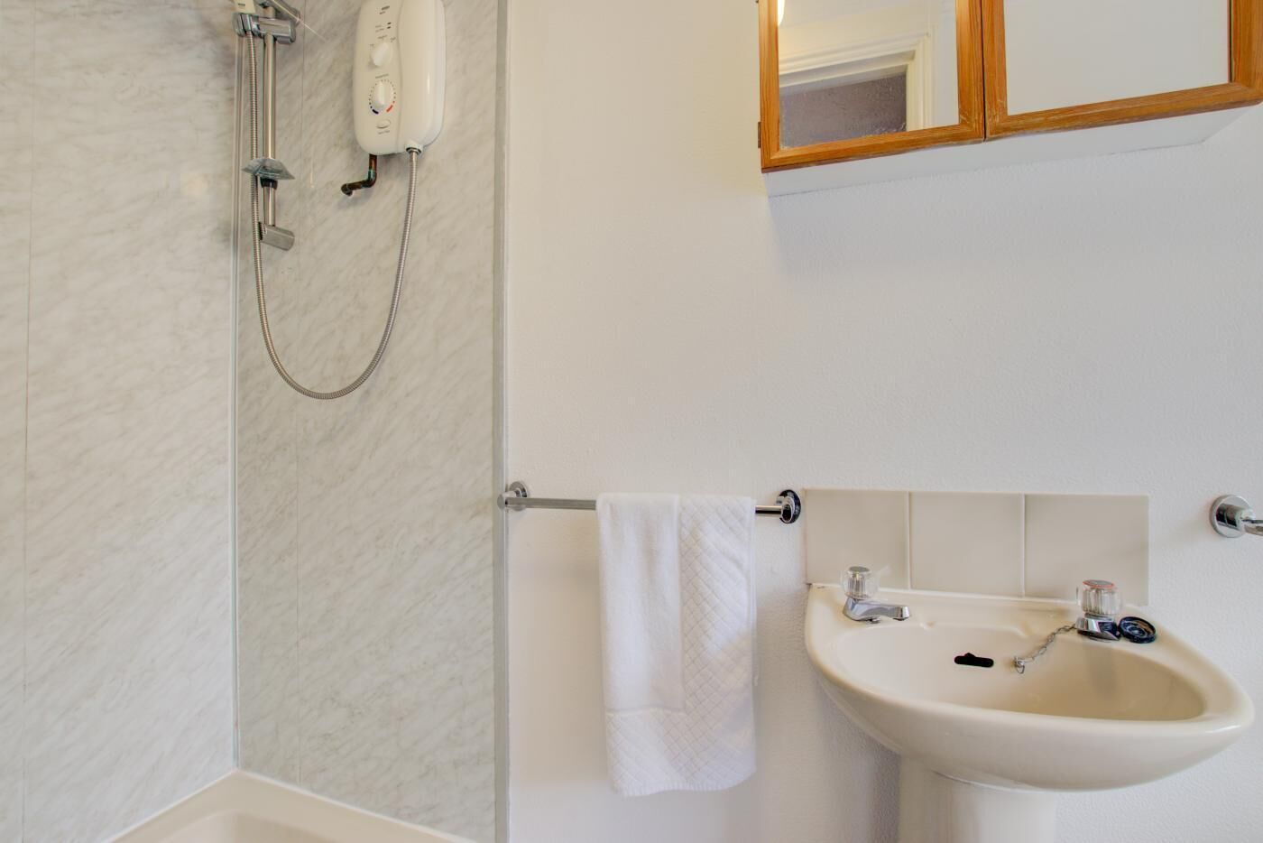 Un baño con ducha, lavabo y toallero.