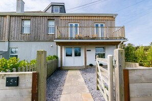 A two-story house with a wooden exterior, a front porch, and a gravel pathway leading to the entrance. - 3 Bed in Little Petherick (oc-p00899) (Little Petherick)