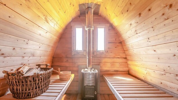 Ein gemütliches Dachzimmer mit Kaminofen, einem Korbwannenstuhl und einer Holzbank.