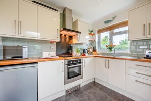 A modern kitchen with white cabinets, stainless steel appliances, and a wooden countertop. - 3 Bed in St. Merryn (oc-p00114) (Saint Merryn)