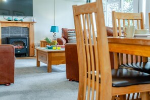 A cozy living room with a fireplace, wooden furniture, and a dining table with chairs. - 3 Bed in St. Merryn (oc-p00114) (Saint Merryn)