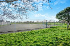 A fenced sports court with a swing set, surrounded by grass and trees. - 3 Bed in St. Merryn (oc-p00114) (Saint Merryn)