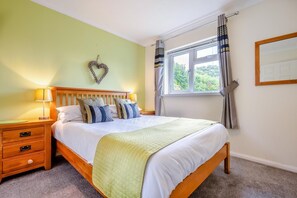 A bedroom with a bed, bedside tables, a window with curtains, and a heart-shaped decoration on the wall. - 3 Bed in St. Merryn (oc-p00114) (Saint Merryn)