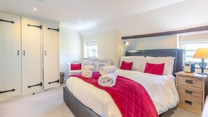 Een slaapkamer met een groot bed, witte muren, een houten hoofdeinde en een raam met zonwering.
