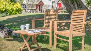 Een houten tafel en twee stoelen in een tuin, met een huis op de achtergrond.