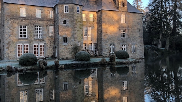 Un bâtiment historique en pierre, doté de nombreuses fenêtres, dont le reflet se mire dans l’eau.