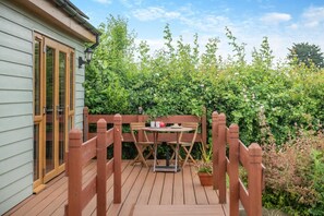 Une terrasse en bois avec une table et des chaises, entourée d’une végétation luxuriante et d’une clôture en bois.
