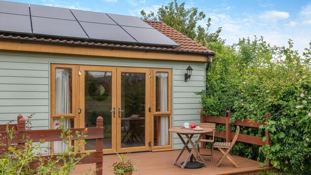 Ett hus med solpaneler på taket, en träveranda och en trädgård.
