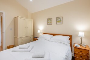 Un lit bien fait, avec du linge de lit blanc et deux oreillers, une table de chevet en bois avec une lampe, une armoire et deux tableaux encadrés au mur.