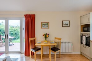 Un espace repas comprenant une table, des chaises, un vase avec des fleurs et une vue sur l’extérieur grâce à une porte vitrée.