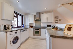 A modern kitchen with white cabinetry, a built-in oven, a dishwasher, and a washing machine. - 2 Bed in Padstow (oc-p00330) (Padstow)