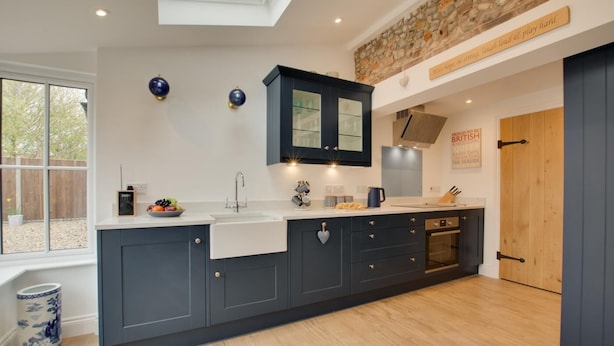 Une cuisine moderne avec des meubles de couleur sombre, une grande fenêtre et un mur d’accent en pierre.