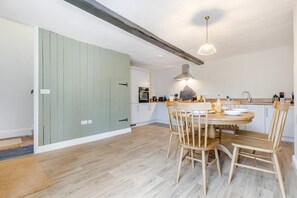 Et moderne køkken med spiseplads, med et rundt træbord, lyse træstole og en hængende lampe over bordet.