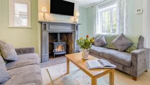 A living room with a fireplace, a sofa, a coffee table with a book, and a TV mounted above the fireplace. - 4 Bed in Bronington (oc-g32599) (Bronington)