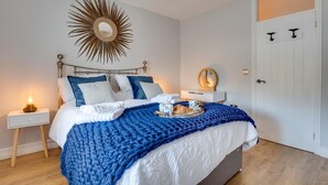 Ein ordentlich bezogenes Bett mit einer blauen Decke, ein Nachttisch mit einer Lampe und ein an der Wand befestigter Spiegel.
