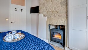 Ein Schlafzimmer mit Kamin aus Stein, einem Bett mit blauer Decke und einer Kaffeetasse sowie Sahnekännchen.
