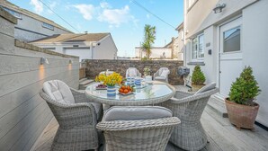 Eine Terrasse mit Korbmöbeln, einem Glastisch und Kübelpflanzen.