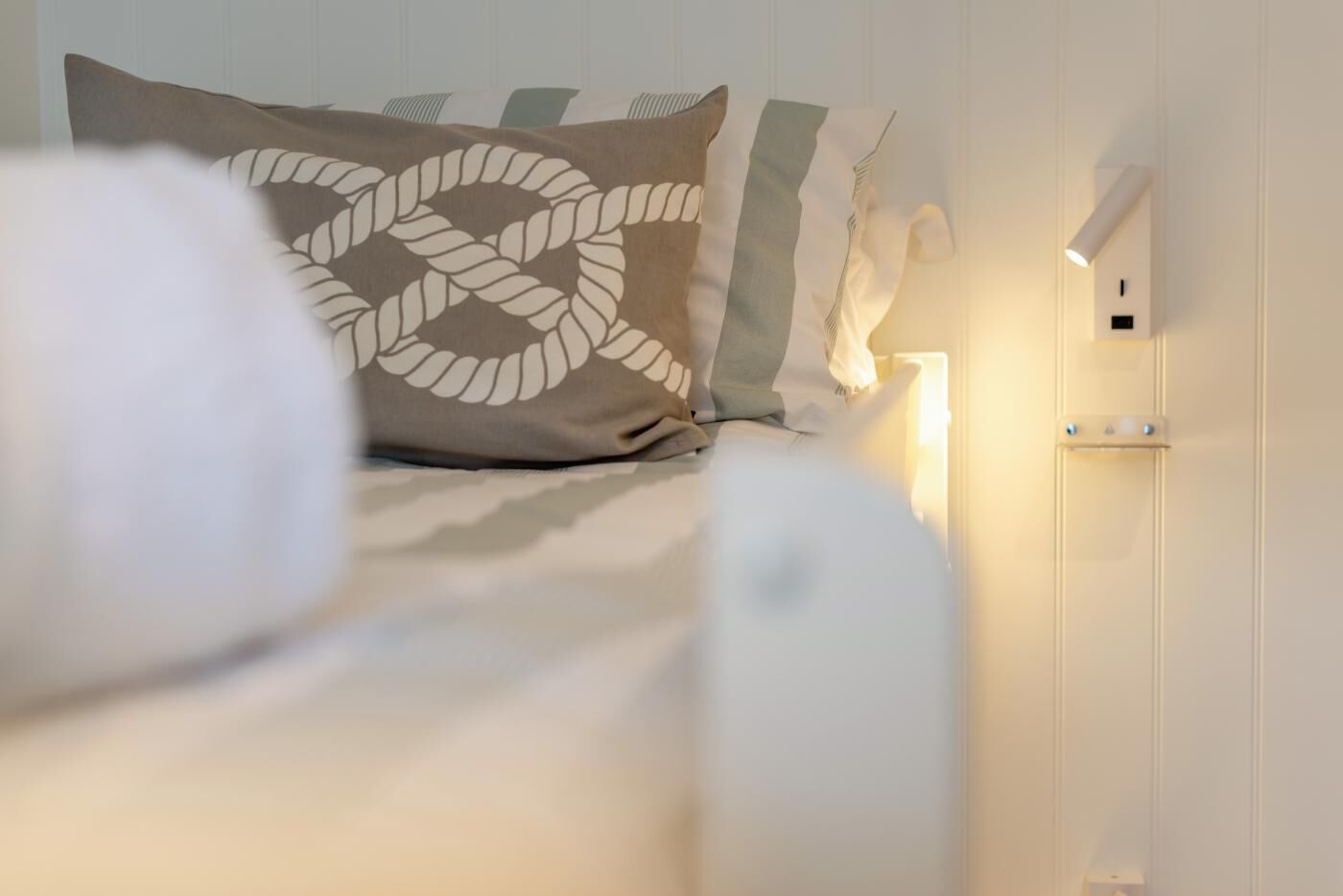 En pænt redt seng med et mønstret pudebetræk og et sengebord med en lampe.
