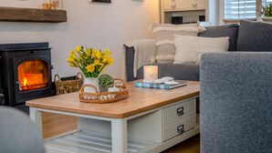 Ein gemütliches Wohnzimmer mit Kamin, einer Couch, einem Couchtisch mit Kerze und einem Blumenkorb.