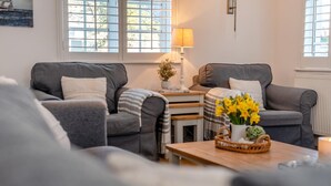 Ein gemütliches Wohnzimmer mit zwei grauen Sofas, einem kleinen Holztisch mit einer Vase voller gelber Blumen und einer Lampe auf einem Beistelltisch.