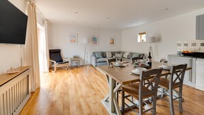 Een moderne woonkamer met een bank, een eettafel gedekt voor twee personen en een keuken met een aanrecht en kastjes.