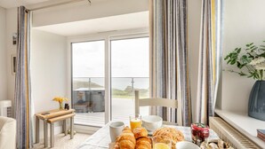 A breakfast setup with croissants, orange juice, and a vase of flowers on a balcony overlooking a scenic view. - 1 Bed in Tintagel (oc-pc084) (Tintagel)