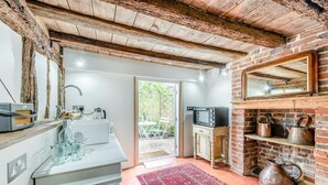 A kitchen with a rustic brick wall, a wooden ceiling, and a red rug. - 2 Bed in Battle (oc-f32643) (Battle)